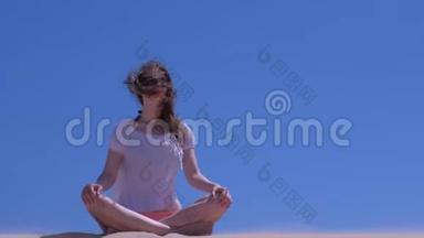 女孩冥想环顾四周，坐在沙滩上的蓝天背景瑜伽姿势。